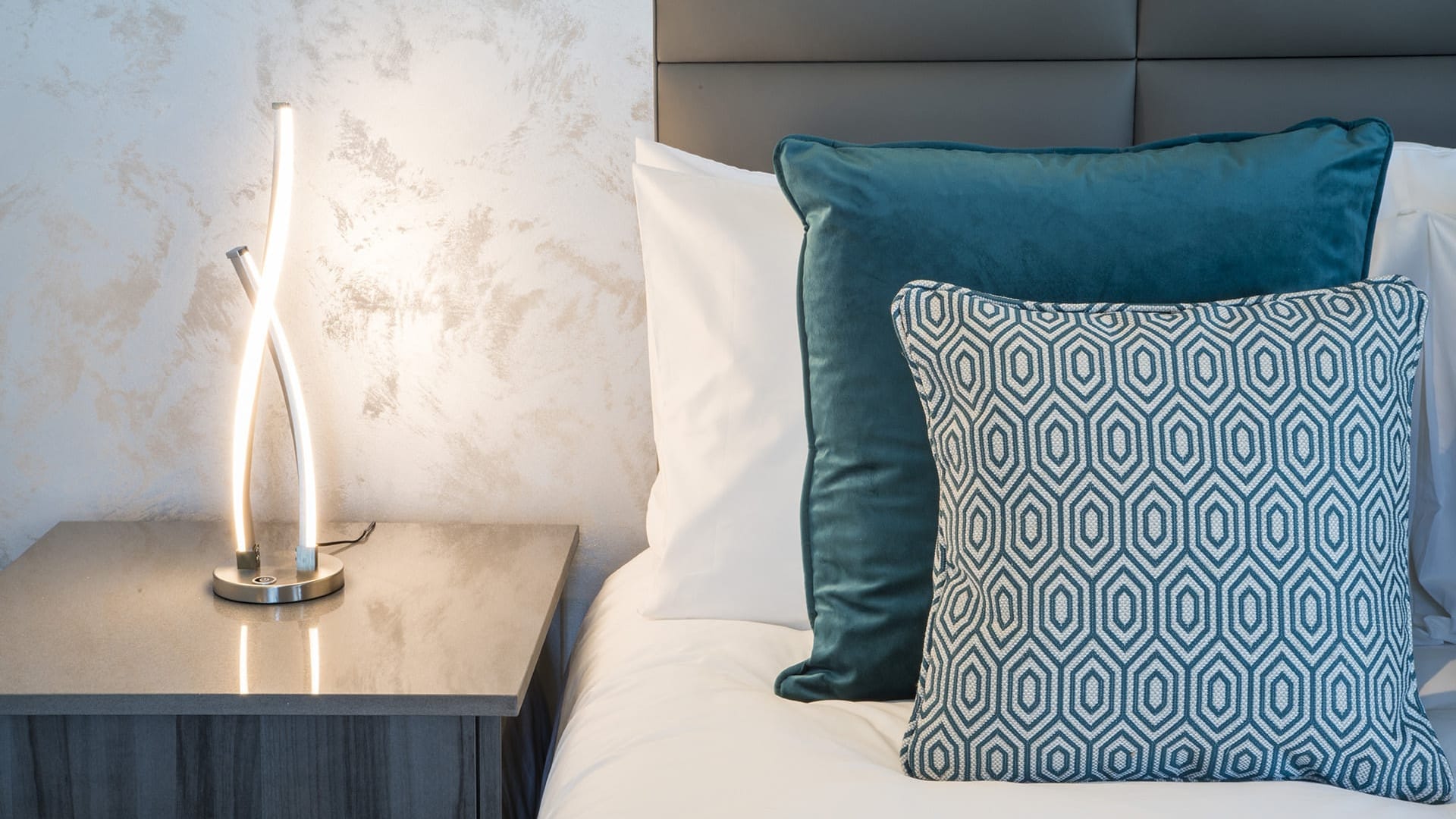 Lamp on table by bed with cushions